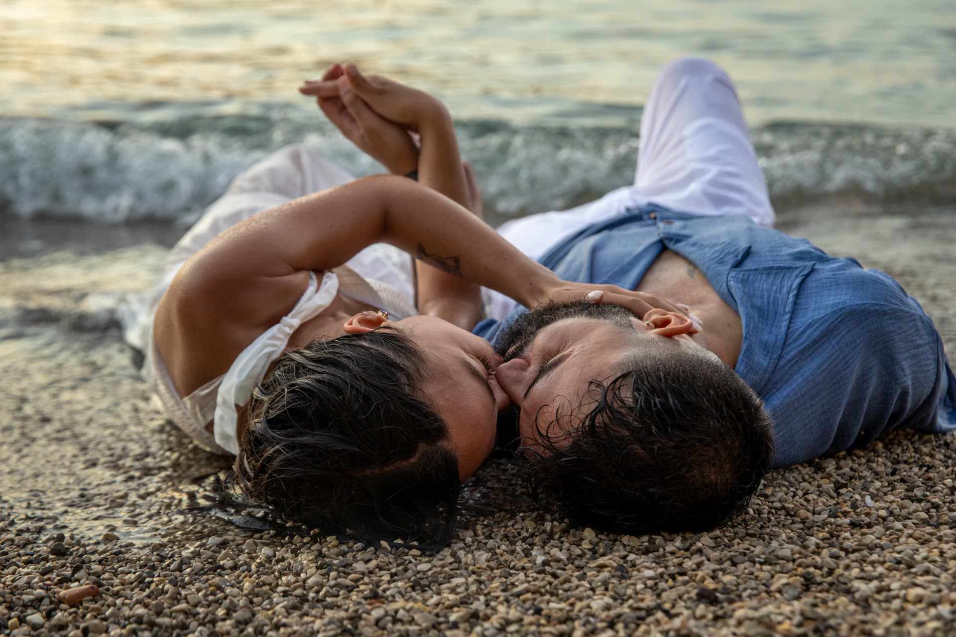 Couple lying on a pebble beach kissing at sunset