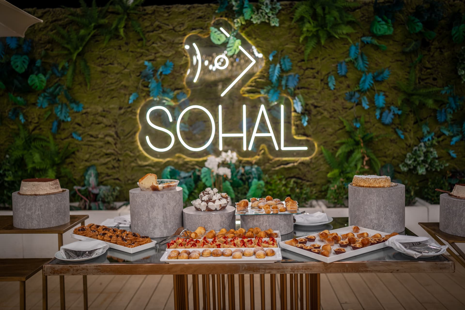 Dessert table with pastries beneath a glowing neon sign
