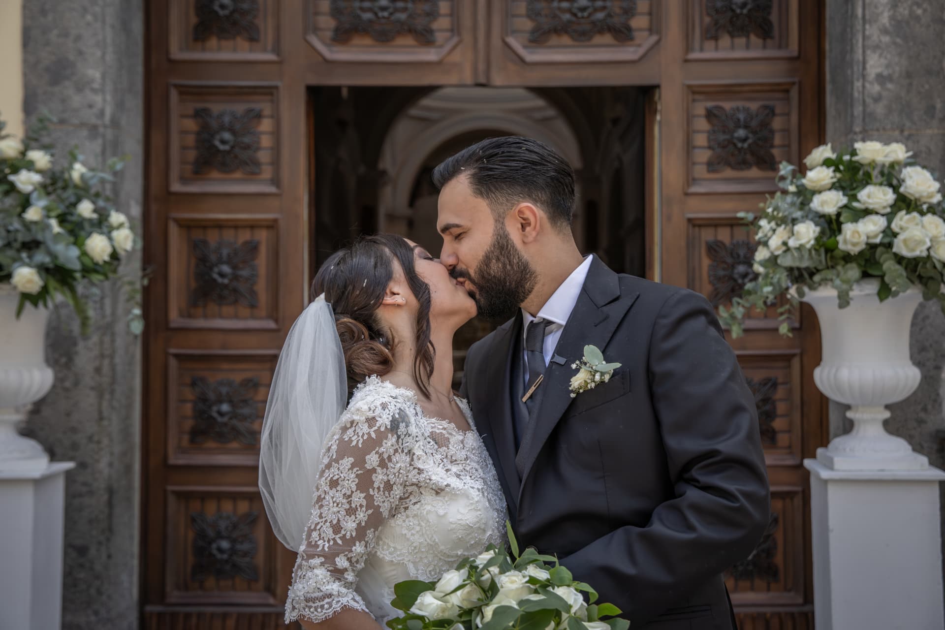 Newlyweds kissing outside a flower-filled church