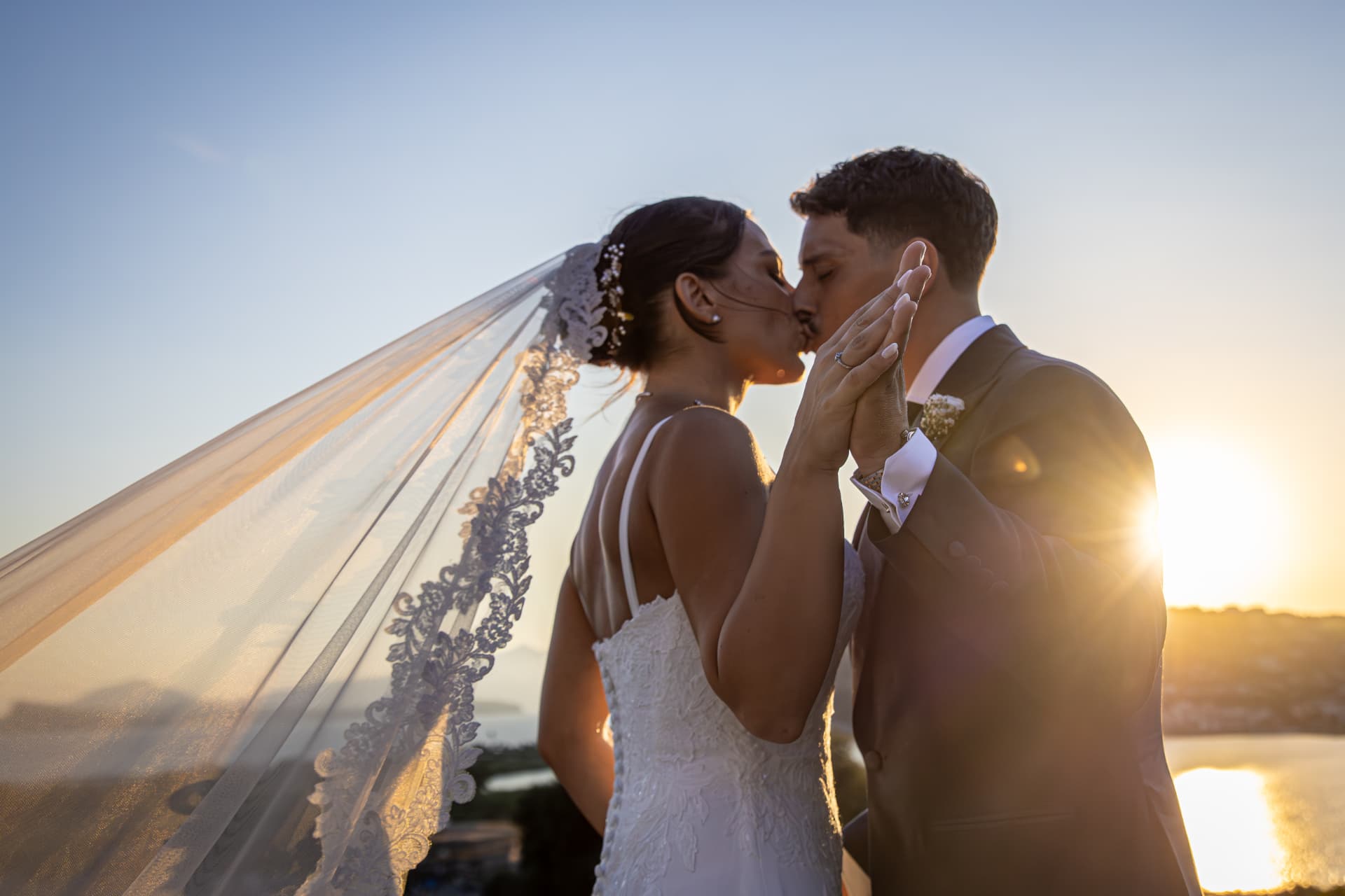 Newlyweds kissing at sunset beneath a lace veil