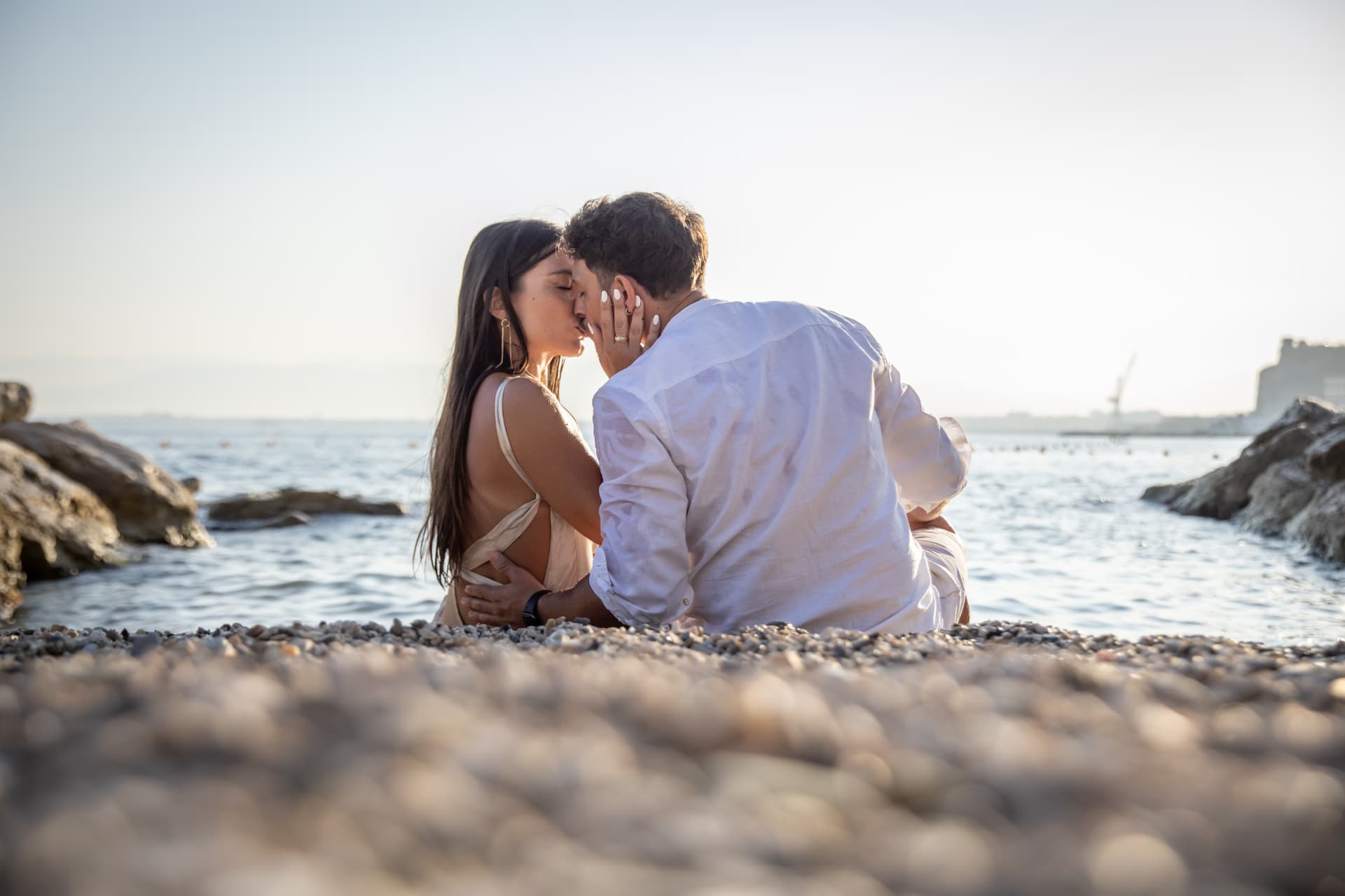 Couple sitting on a pebble beach kissing by the sea