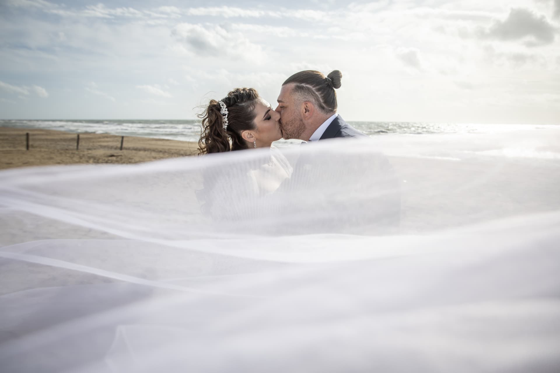 Newlyweds kissing on the beach beneath a flowing veil