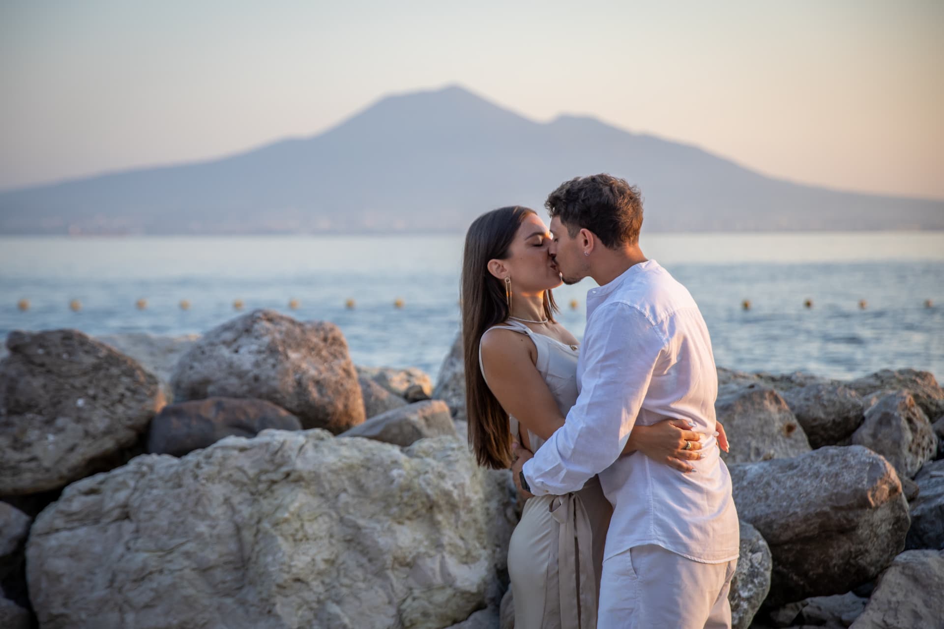 Couple kissing on rocky shore with a volcano on the horizon
